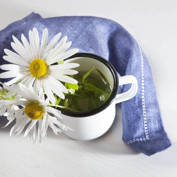 Margaritas en una taza de esmalte blanco y una servilleta azul sobre una mesa de madera blanca —  Fotos de Stock