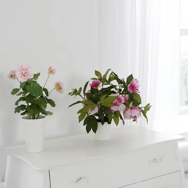 Den konstgjorda geranium och pioner i krukor på en vit byrå som en dekoration i rummet — Stockfoto