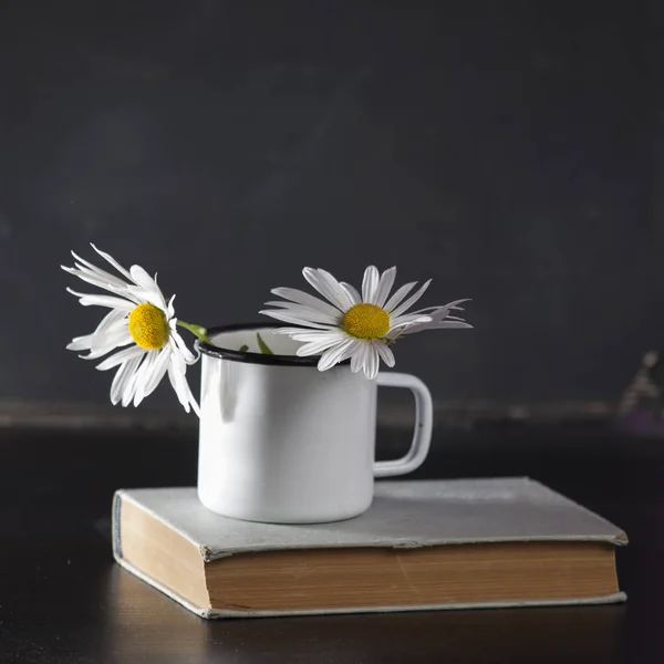 Las Margaritas en la taza blanca de esmalte sobre el fondo de papel negro —  Fotos de Stock