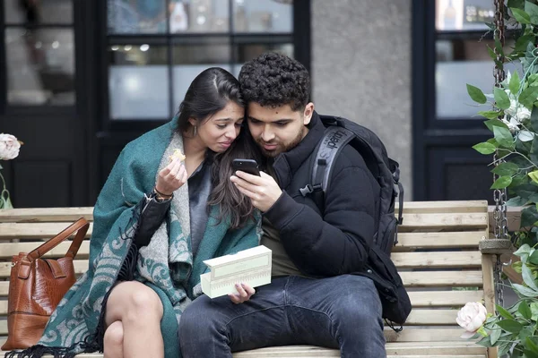 Счастливые пары смотрят в телефоны, сидя на скамейке возле Ковент-Гарден — стоковое фото