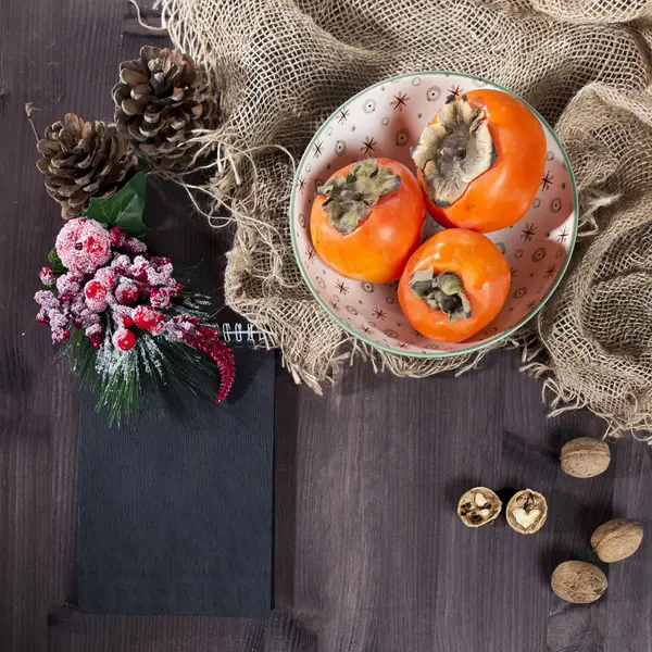 El caqui en el plato sobre la servilleta hecha de la lona sobre la mesa oscura de madera —  Fotos de Stock