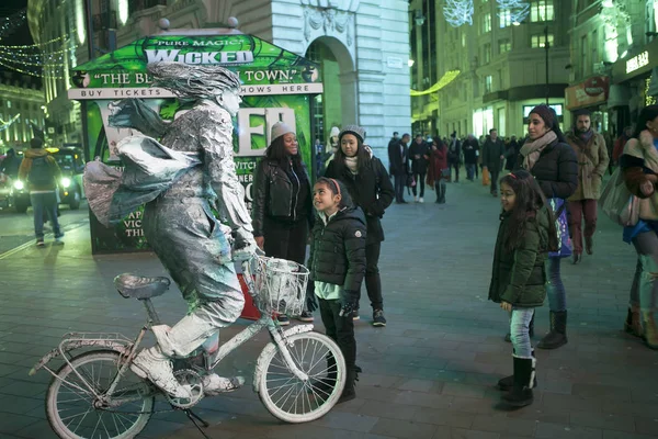 Una figura viva es un hombre con pintura plateada en una bicicleta en Piccadilly en Londres al atardecer. —  Fotos de Stock