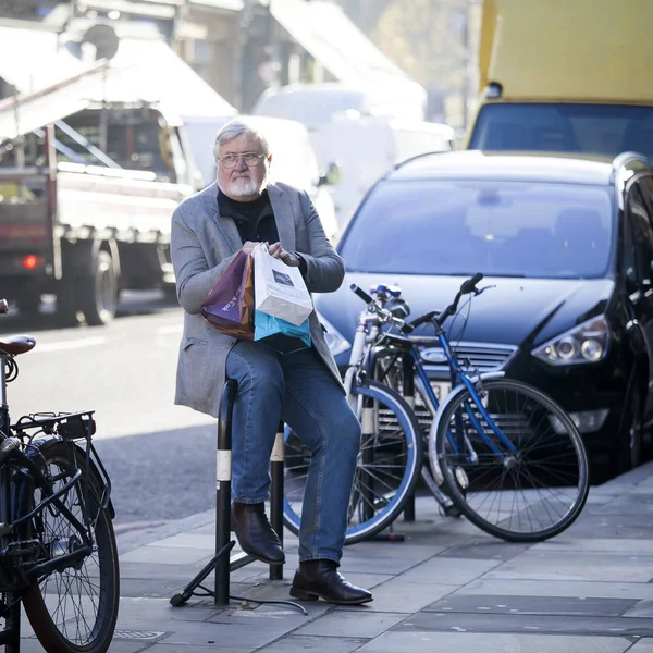 Un anciano con gafas se sienta cerca de Liverpool Street, descansando de las compras — Foto de Stock