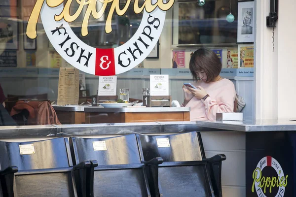 Mädchen im rosafarbenen Pullover an einem Tisch in einem Café schaut in ihr Handy, während sie auf Essen wartet — Stockfoto