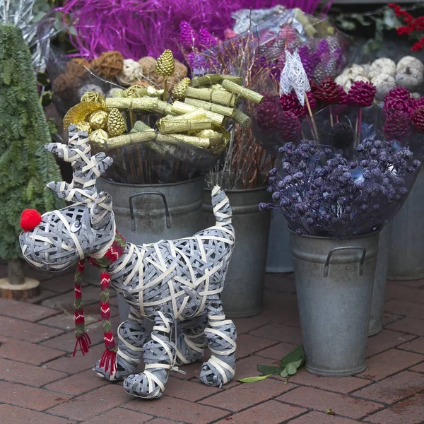 A bucket with gilded cinnamon and cones for sale on the flower market. Wicker dog from the vine next to the bucket — Stock Photo, Image
