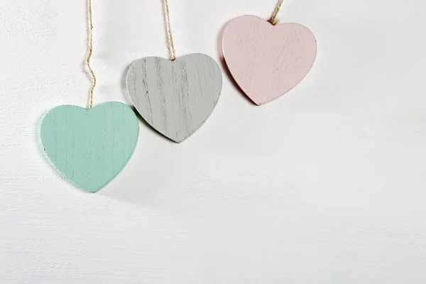 Tři dřevěné srdce visí na bílé dřevěné stěně — Stock fotografie