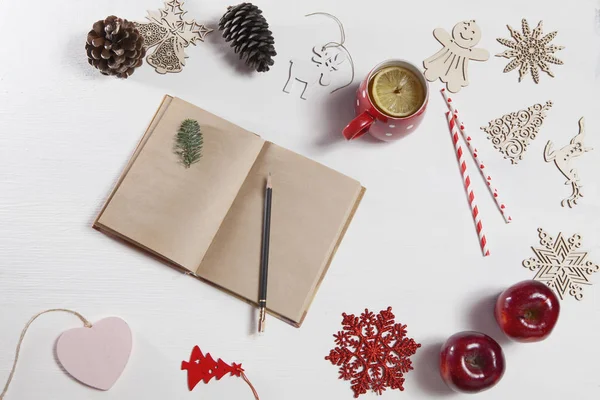 Manos de una mujer que va a dibujar a lápiz en cuaderno. En la mesa hay una taza de té con limón, copo de nieve, juguetes de Navidad y manzana —  Fotos de Stock