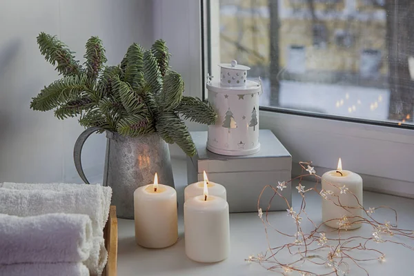 Las ramas de un árbol de Navidad en una jarra de zinc en la ventana. La guirnalda está encendida y las velas arden . — Foto de Stock