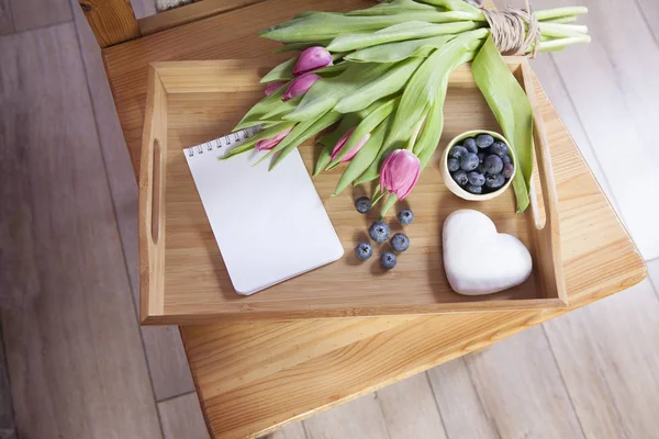 Tray with tea and gingerbread in the shape of heart and a bouquet of tulips on the chair — Stock Photo, Image