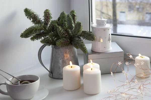 Os ramos de uma árvore de Natal em um jarro de zinco na janela. A grinalda está acesa e as velas estão a arder . — Fotografia de Stock