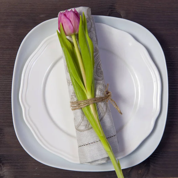 Z życzeniami na Walentynki. Dekoracje weselne. Biała płyta serwetka z tulipana pięknie przywiązane. Drewniany stół brązowy — Zdjęcie stockowe