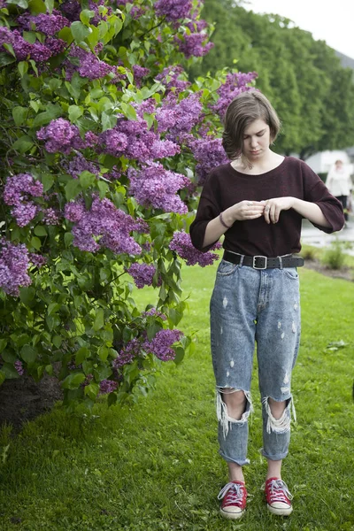 Pensive tyttö poseeraa lila pensaita puistossa — kuvapankkivalokuva