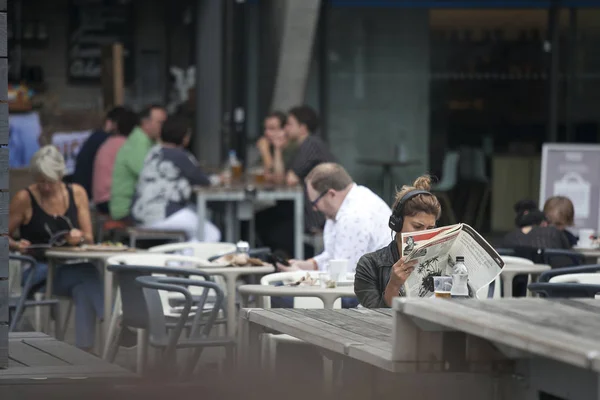 Una ragazza legge una rivista, ascolta musica e beve birra in un caffè — Foto Stock