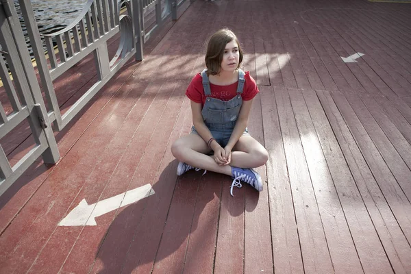 Jong meisje in een rode wollen trui en jeans broek zit op de pier — Stockfoto