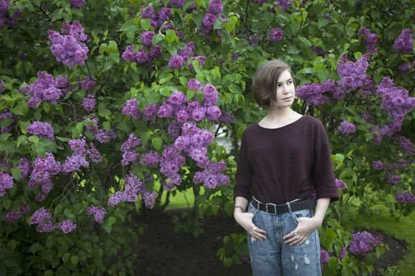 Chica pensativa posando en arbustos lila en el parque —  Fotos de Stock