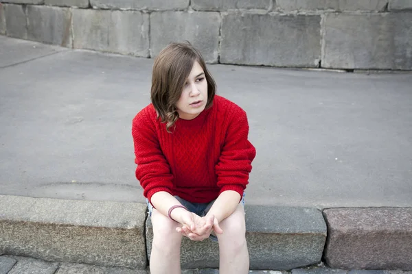 Mladá dívka v červených vlněný svetr a džíny kraťasy sedí na schodech — Stock fotografie