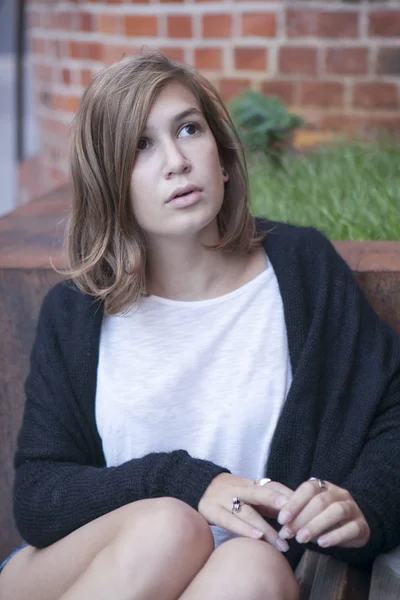 Thoughtful girl in a long black cardigan and short shorts is sitting on the steps — Stock Photo, Image