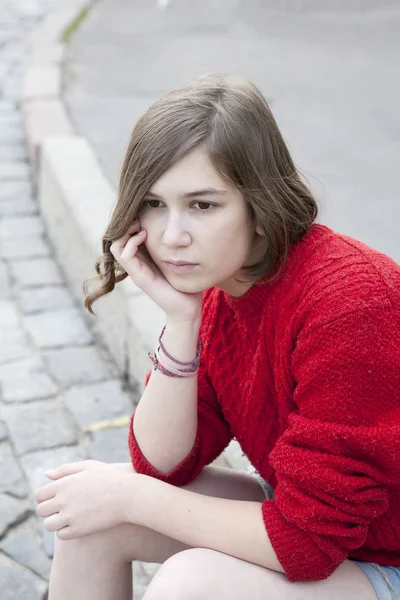 Joven chica en un suéter de lana roja y pantalones cortos jeans está sentado en las escaleras —  Fotos de Stock