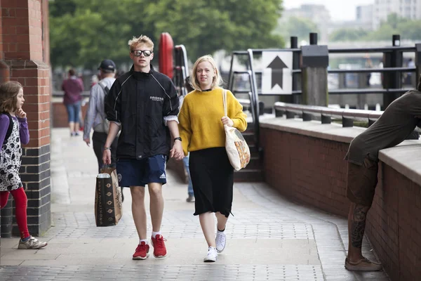 A girl in an orange sweater and a black skirt walks with her boy along — Stock Photo, Image