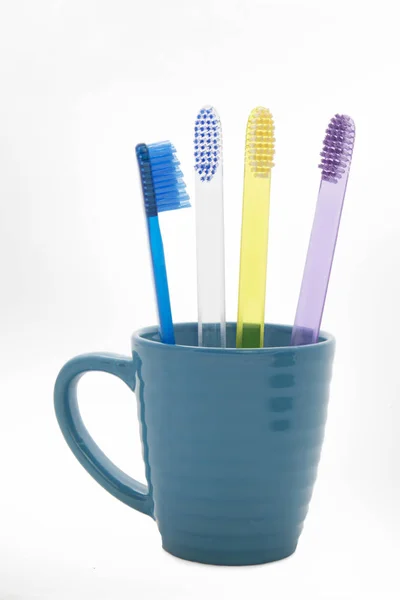 Cuatro cepillos de dientes multicolores en un vaso azul —  Fotos de Stock