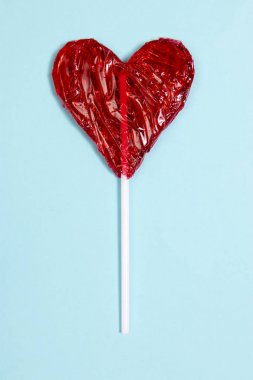 kalp şeklinde koyu mavi zemin üzerine kırmızı lolipop şeker.