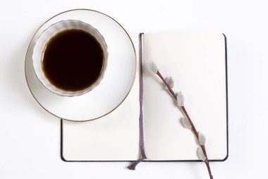 Beyaz fincan kahve üstünde beyaz bir defter ve bir beyaz ahşap masa söğüt dalına.