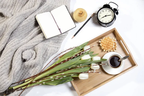 Tablett mit Kaffee, weißen Tulpen und Weiden steht auf dem Bett. Der Wecker zeigt sieben Uhr morgens. — Stockfoto