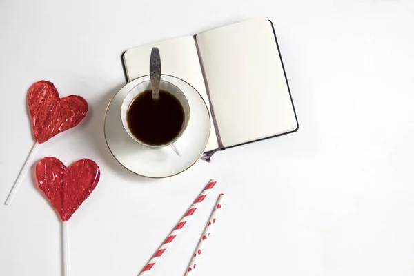 En kopp kaffe med en anteckningsbok och två godis i form av ett hjärta på ett träbord. Kort för alla hjärtans dag, mors dag — Stockfoto