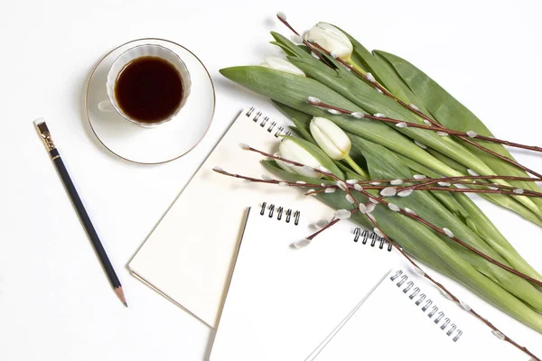 La taza blanca de café en un cuaderno blanco, tulipanes blancos, una rama de sauce en una mesa de madera blanca. Copiar espacio —  Fotos de Stock