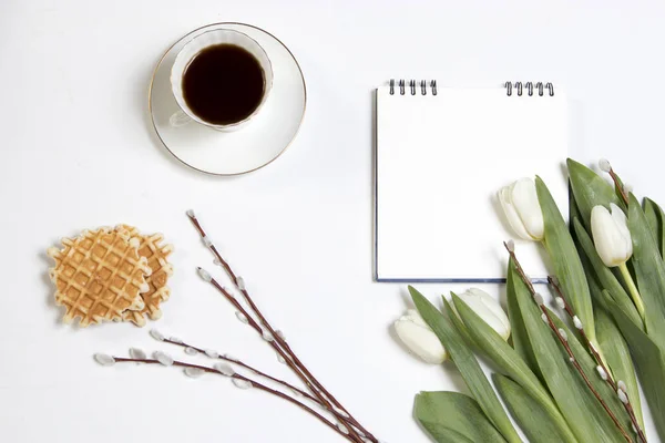 Vit kopp kaffe på en vit anteckningsbok, Vita tulpaner, en willow gren på en vit träbord. Kopiera utrymme — Stockfoto
