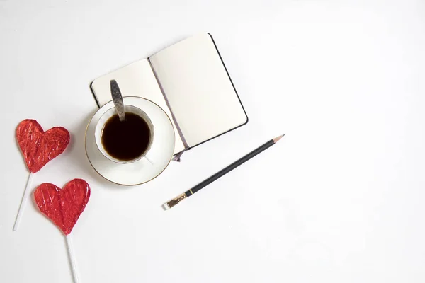 En kopp kaffe med en anteckningsbok och två godis i form av ett hjärta på ett träbord. Kort för alla hjärtans dag, mors dag — Stockfoto