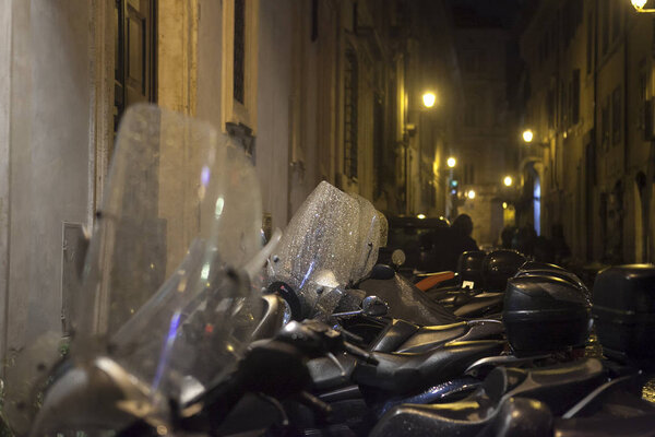Motorcycles parked against the wall in the light of street lamps