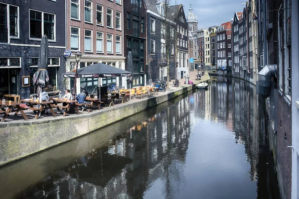 Typische oude Amsterdam gebouwen langs het kanaal. Mensen op de bankjes. Tulpen in kuipen — Stockfoto