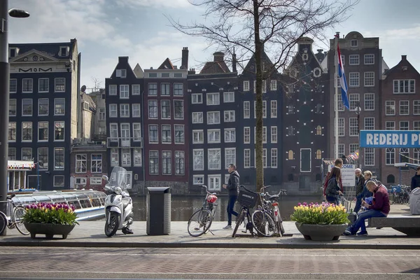 Typische oude Amsterdam gebouwen langs het kanaal. Mensen op de bankjes. Tulpen in kuipen — Stockfoto