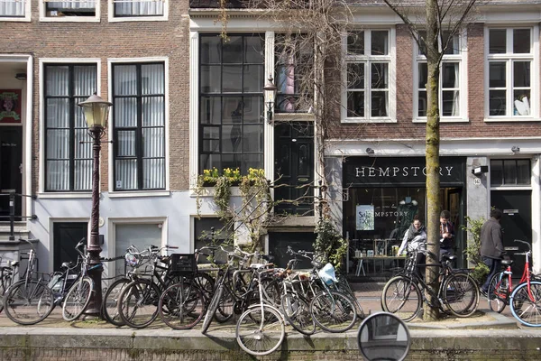Típicos edificios antiguos de Ámsterdam a lo largo del canal. Gente en los bancos. Tulipanes en tinas — Foto de Stock