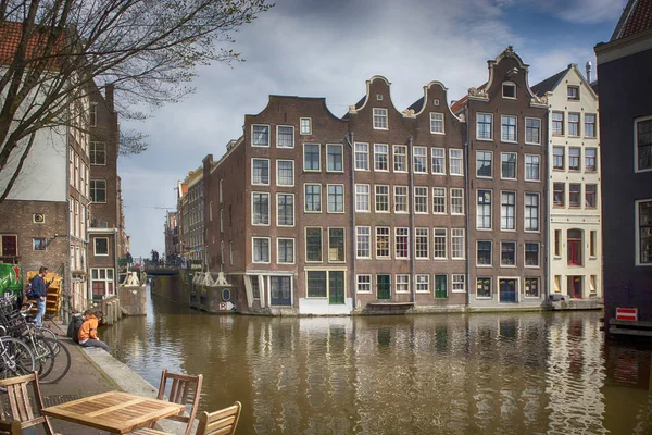 Edifícios típicos de Amesterdão ao longo do canal. Pessoas nos bancos. Tulipas em banheiras — Fotografia de Stock