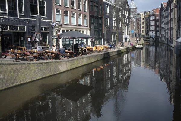 Typische oude Amsterdam gebouwen langs het kanaal. Mensen op de bankjes. Tulpen in kuipen — Stockfoto