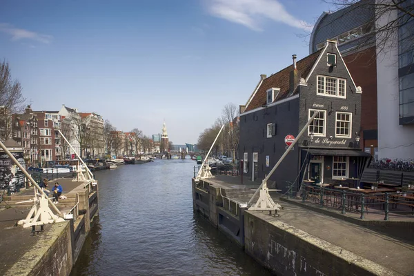 Tipici vecchi edifici di Amsterdam lungo il canale. Gente sulle panchine. Tulipani in vasche — Foto Stock