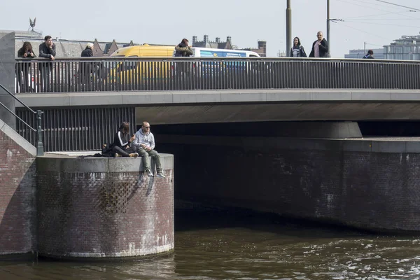 Een gelukkige paar zit op een brug, opknoping van hun benen in de Amstel — Stockfoto