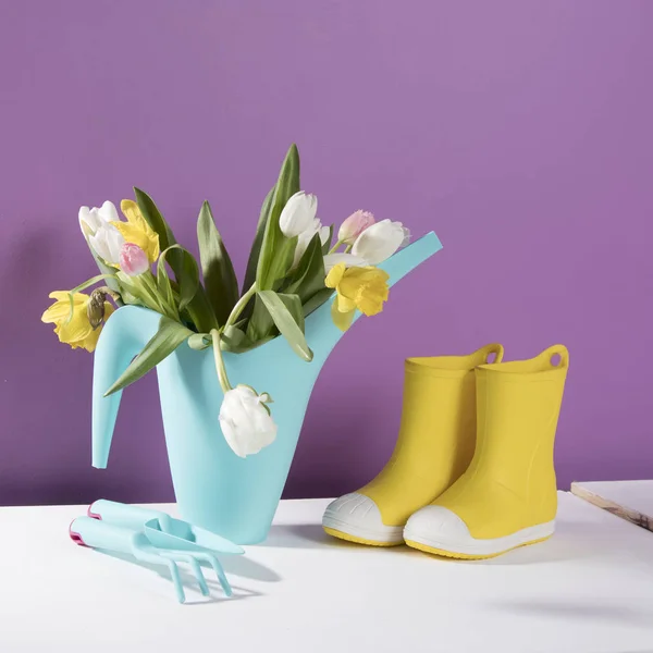 The Yellow rubber boots with a bouquet of flowers of yellow daffodils and white and pink tulips. Garden accessories. — Stock Photo, Image
