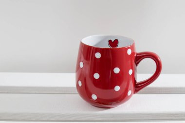 Kırmızı puantiyeli kupa güneşli bir günde beyaz bir rafta duruyor..