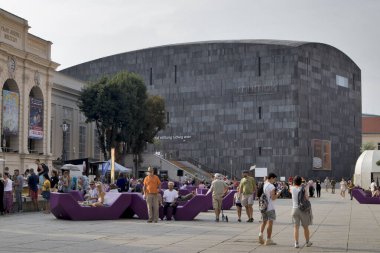 Viyana sanat pavyonu ve Mumok Müzesi. İnsanlar konserleri dinler, sandalyelerde oturur, mor banklarda uzanır..