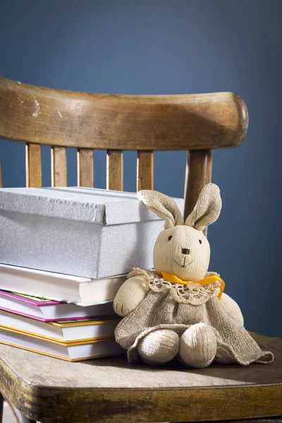 Speelgoed doek haas in een grijze jurk zit op een houten stoel. — Stockfoto