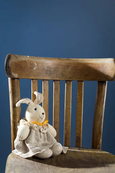 Speelgoed doek haas in een grijze jurk zit op een houten stoel. — Stockfoto