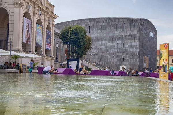 Wiedeński pawilon sztuki i Mumok Museum. Ludzie słuchają koncertów, siedzą na krzesłach, leżą na fioletowych ławkach. — Zdjęcie stockowe