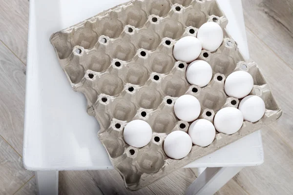 Des œufs de poulet dans un récipient en carton blanc reposent sur une table de cuisine en bois beige . — Photo