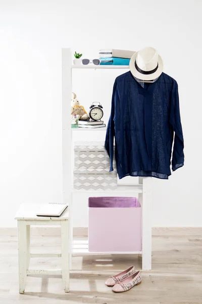 Storage system in the bedroom. Shelving with boxes, alarm clock, books, for small items and with dress hanging on a hanger