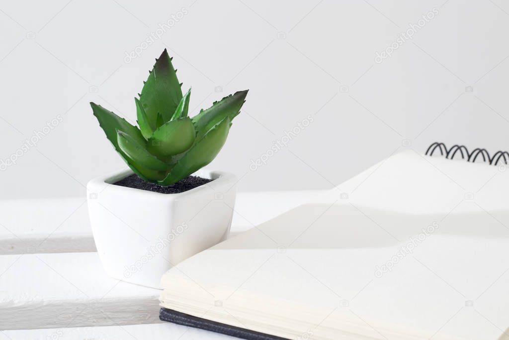 Artificial succulent in a white ceramic pot a rack against the background of a notebook.