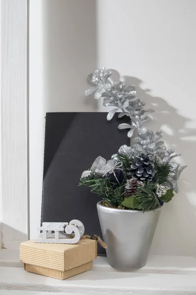 Composizione natalizia con rami di abete in una pentola grigia, con blocco note e una confezione regalo con piccole slitte — Foto Stock