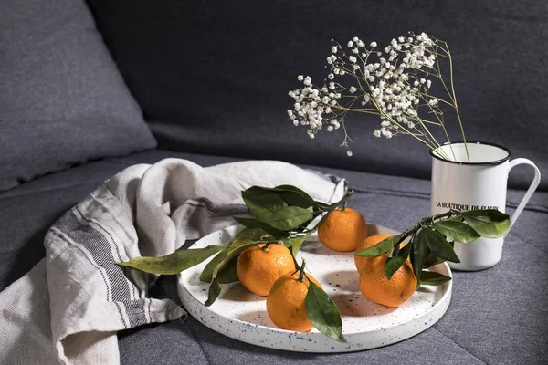 Mandarinas con hojas verdes en plato de cerámica blanca con una toalla de cocina gris —  Fotos de Stock